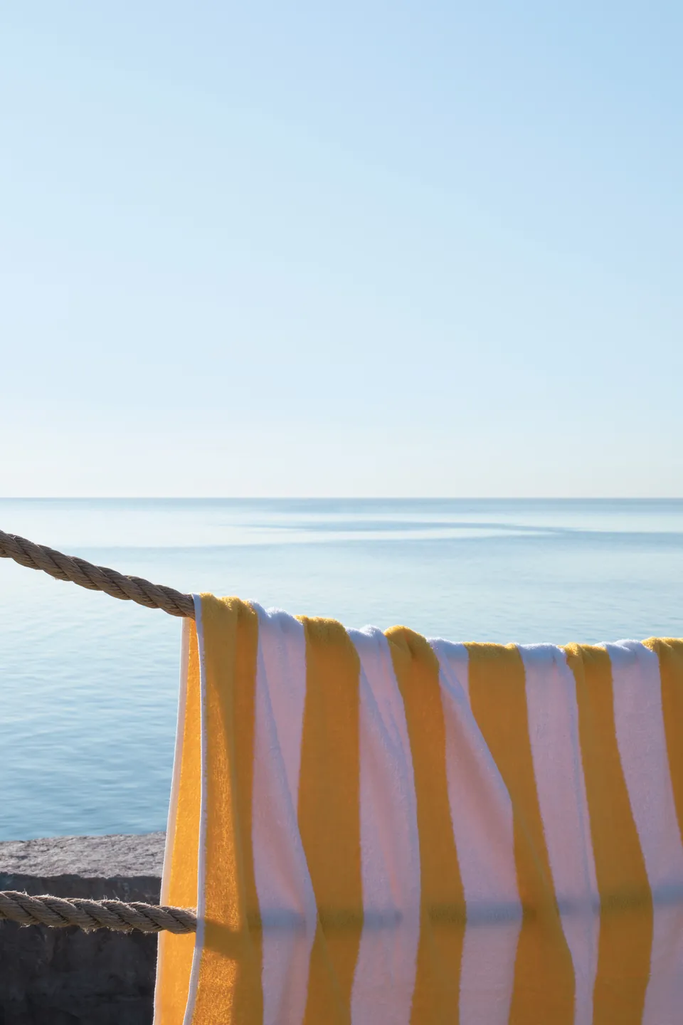 A striped beach towel drying in the sun by the water